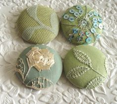 four different colored buttons sitting on top of a white cloth covered tablecloth with flowers and leaves