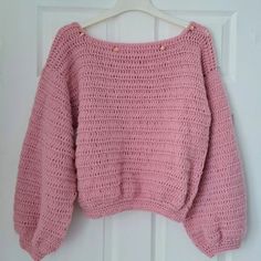 a pink sweater hanging up on a white door hanger, with the top half crocheted