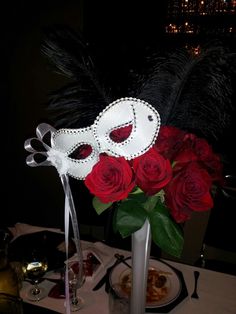 a table topped with a vase filled with red roses and a white mask