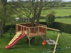 a wooden play set in the middle of a grassy area with a slide and climbing frame