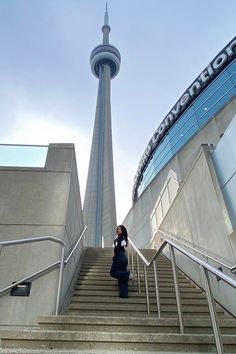 a woman is standing at the top of stairs in front of a building with a sky scraper behind her