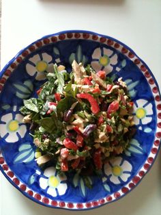 a blue and red bowl filled with salad on top of a white table next to a knife