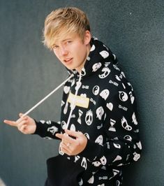 a young man leaning against a wall wearing a black and white hoodie