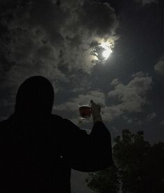 a man is holding up his cell phone at night with the moon in the background