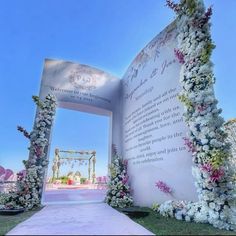 an outdoor wedding ceremony setup with flowers on the side and a large white sign in the middle