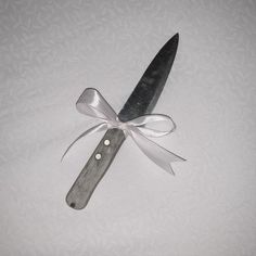 a knife with a ribbon tied around it on a white tableclothed surface, ready to be used as an ornament