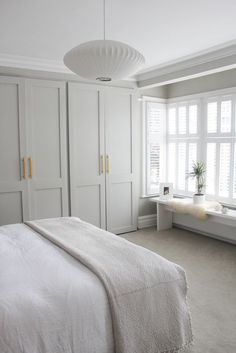 a white bed sitting in a bedroom next to a window filled with lots of windows