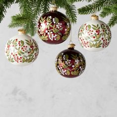 three ornaments hanging from a christmas tree with leaves and berries painted on them in red, white and green colors