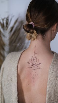 the back of a woman's neck with a cross and lotus tattoo on it