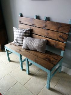 a wooden bench sitting next to a wall with two pillows on it's back