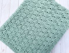 a green crocheted blanket sitting on top of a white wooden floor next to a pair of scissors