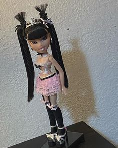 a doll is standing on top of a black table and wearing a pink dress with feathers