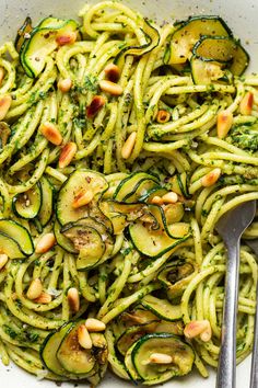 zucchini pasta with pesto and pine nuts in a white bowl next to a fork