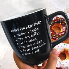 a hand holding a black coffee mug with donuts on the table in the background