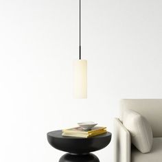 a white couch sitting next to a table with a book on it and a lamp hanging from the ceiling