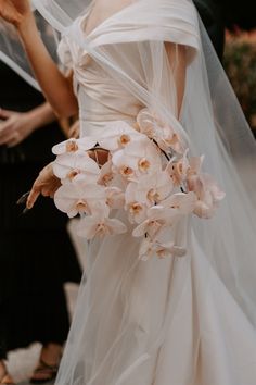 a woman in a wedding dress holding a bouquet of flowers with veil over her head