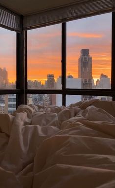 an unmade bed in front of a window with the city skyline seen through it