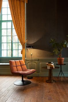 an orange chair and table in front of a window with curtains on the windowsill