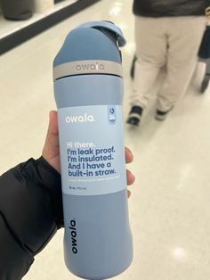 someone holding up a water bottle in the middle of an airport terminal with other people walking by