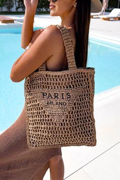 a woman wearing a hat and carrying a bag by a swimming pool with the words paris on it