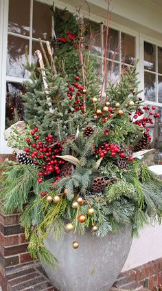 a planter filled with evergreen, pine cones and red berries