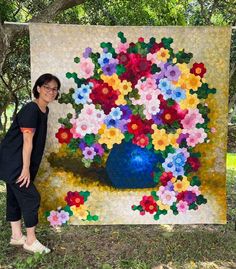 a woman standing next to a large quilt with flowers on it and a blue vase