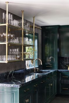 a kitchen with green cabinets and marble counter tops, gold trimmings on the shelves