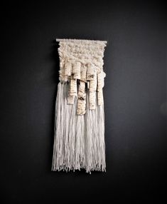 the wall hanging is made out of wood and white yarn with tassels on it