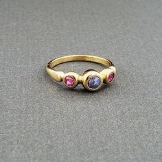 This dainty handmade ring is 14k gold featuring two lovely little rubies and a gorgeous lightly colored sapphire. A great ring for everyday wear! Gold Multi-stone Pink Sapphire Ring, Three Stone Pink Sapphire Jewelry Gift, Luxury Gold Ruby Three Stone Ring, Luxury Gold Three-stone Ruby Ring, Luxury Gold Three Stone Ruby Ring, Luxury Gold Ruby Ring With Three Stones, Gold Pink Sapphire Ring In Round Cut, Yellow Gold Ruby Ring With Three Stones, Yellow Gold Three Stone Ruby Ring