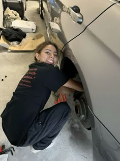 a woman is working on the side of a car with her hands in the wheel