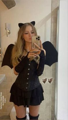 a woman taking a selfie in front of a bathroom mirror with a bat costume on