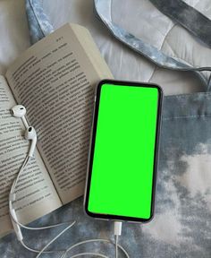 an open book and headphones are sitting on a bed next to a cell phone