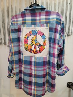 a plaid shirt with a peace sign patch on the front and flowers in the middle