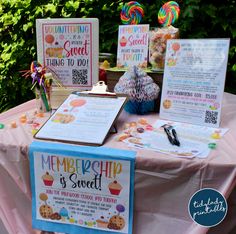 a table topped with menus and candy bar signs on top of a pink cloth covered table