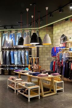 the inside of a clothing store with clothes on racks and lamps hanging from the ceiling