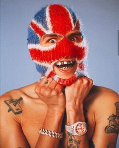 a shirtless man wearing a knitted union jack mask and bracelets on his face