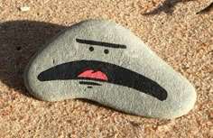 a rock with a face painted on it sitting in the sand next to another rock