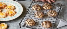 some cookies are on a cooling rack next to a white plate with oranges and other pastries