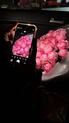 a person holding a cell phone in front of a bouquet of pink roses