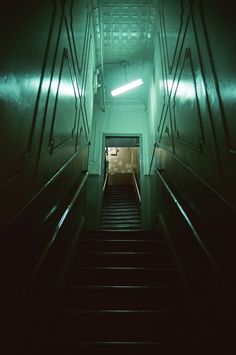 stairs leading up to the top of a flight of stairs in a dark room with light coming from above