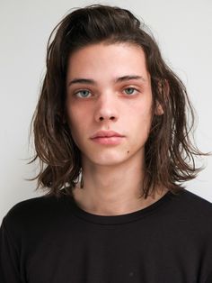 a young man with long hair wearing a black t - shirt looking at the camera