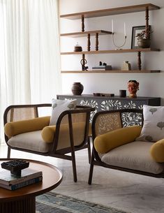 a living room with two chairs and a table in front of a wall mounted shelf