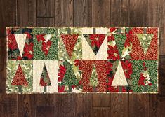 a quilted table runner with poinsettis and holly on it, sitting on a wood floor