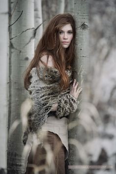 a woman standing next to a tree with her arms wrapped around the back of it