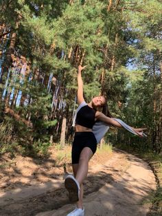 a woman in black shorts and white shirt doing a trick on a skateboard with trees in the background