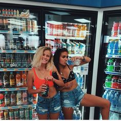 two women standing in front of a refrigerator with drinks on it and one woman taking a selfie