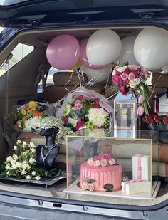 the back of a car with balloons, flowers and cake in it's trunk