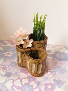 two flower pots with flowers in them on a tableclothed surface, one is made out of wood and the other has grass growing from it