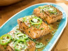 two pieces of fish on a blue plate with green peppers and seasoning sprinkles