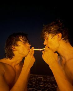 two young men standing next to each other with toothbrushes in their mouths and one is brushing his teeth